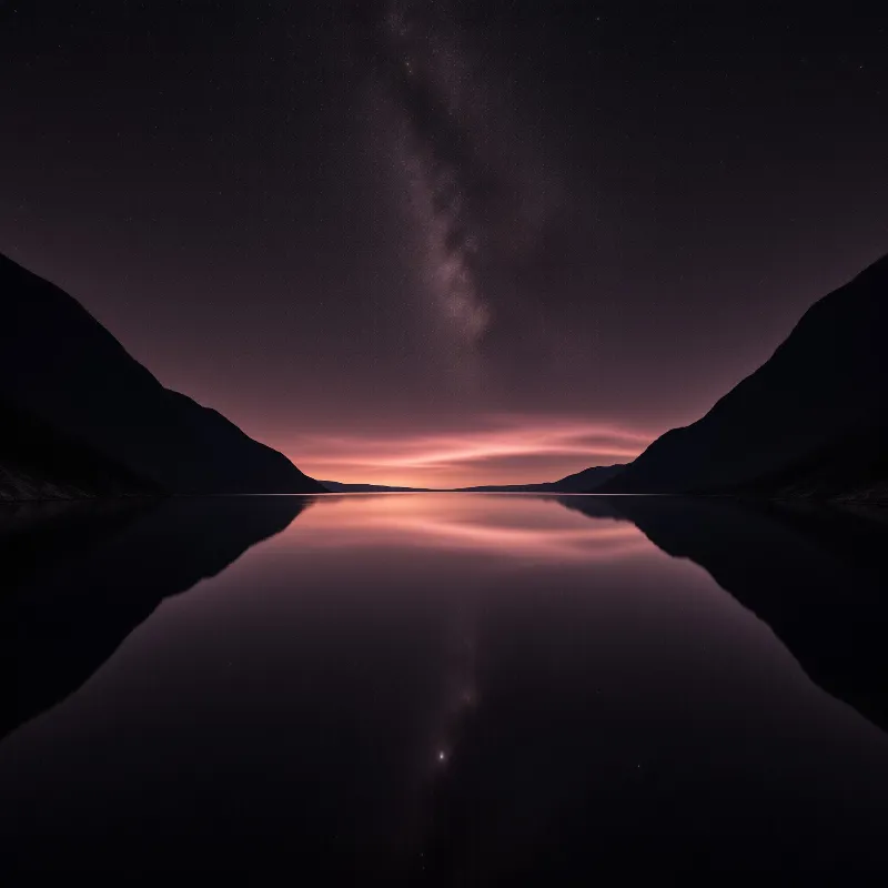 A vertical band of stars and galactic dust reflects in calm water between dark mountain silhouettes at night.