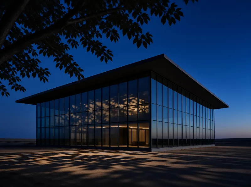 A minimalist glass-walled building lit from within stands under a deep blue dusk sky.
