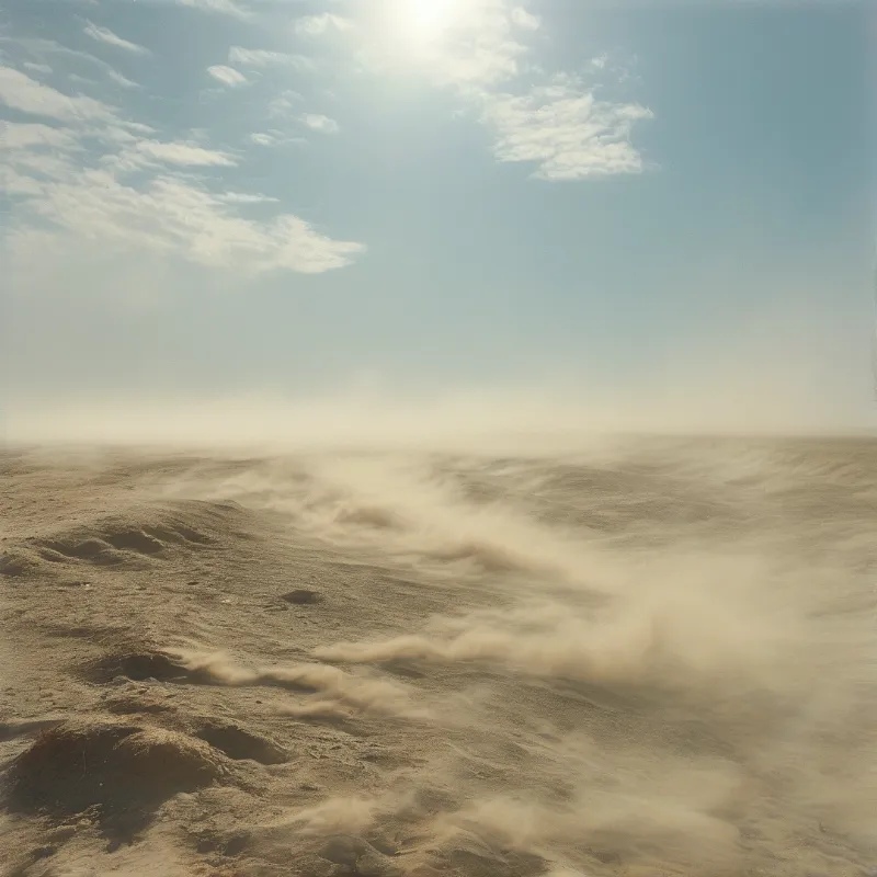 A wide expanse of sandy terrain with blowing dust and a hazy sky under a bright sun.