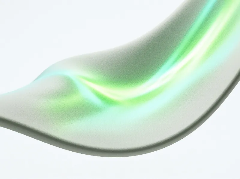 A curving iridescent metal band with pale green and white light reflections rests against a plain white surface.