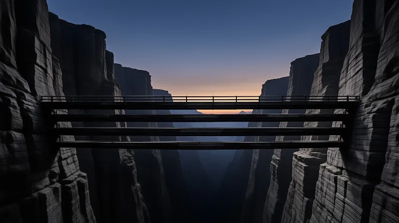 A long straight bridge crosses a deep rocky gorge as the sky glows with warm orange light at the horizon.