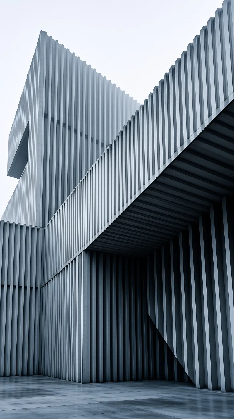 Low angle view of a massive grey concrete building with tall vertical ribs receding into a dark passage under a pale sky.