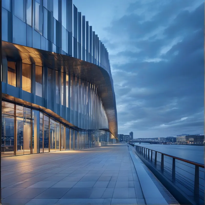 A contemporary building with a reflective glass exterior stands beside a calm river under a cloudy twilight sky.
