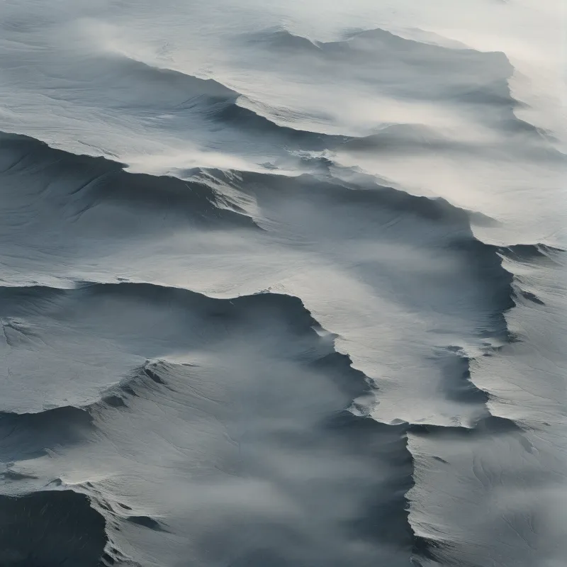 An aerial view of snow covered peaks with misty layers and soft shadows.