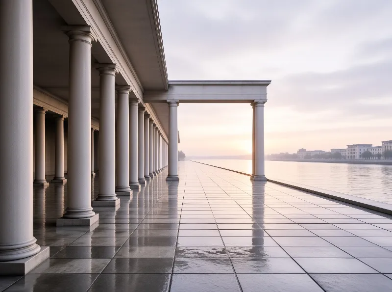 A long row of white classical columns stands beside a calm river reflecting the warm light of early morning.