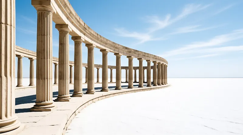A curved fluted stone colonnade stretches across an empty bright white ground under a clear blue sky with faint wispy clouds.