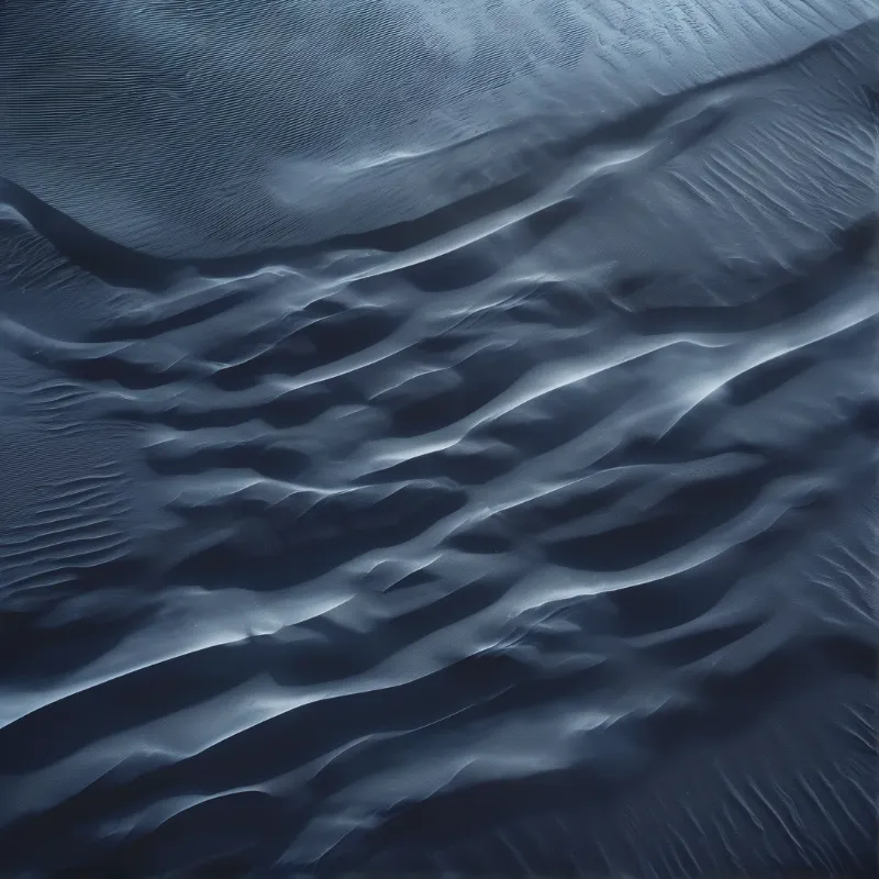 An image of undulating blue dune ripples catches strong light, creating deep shadows across the textured surface.