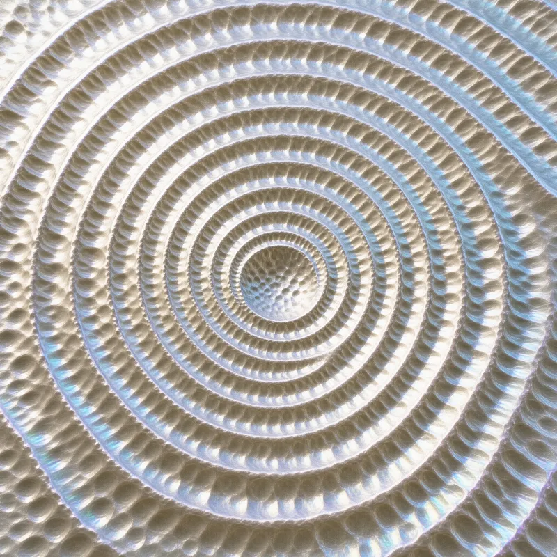 A close-up view of a silver spiral object with a dimpled surface that shimmers with iridescent colors under bright illumination.