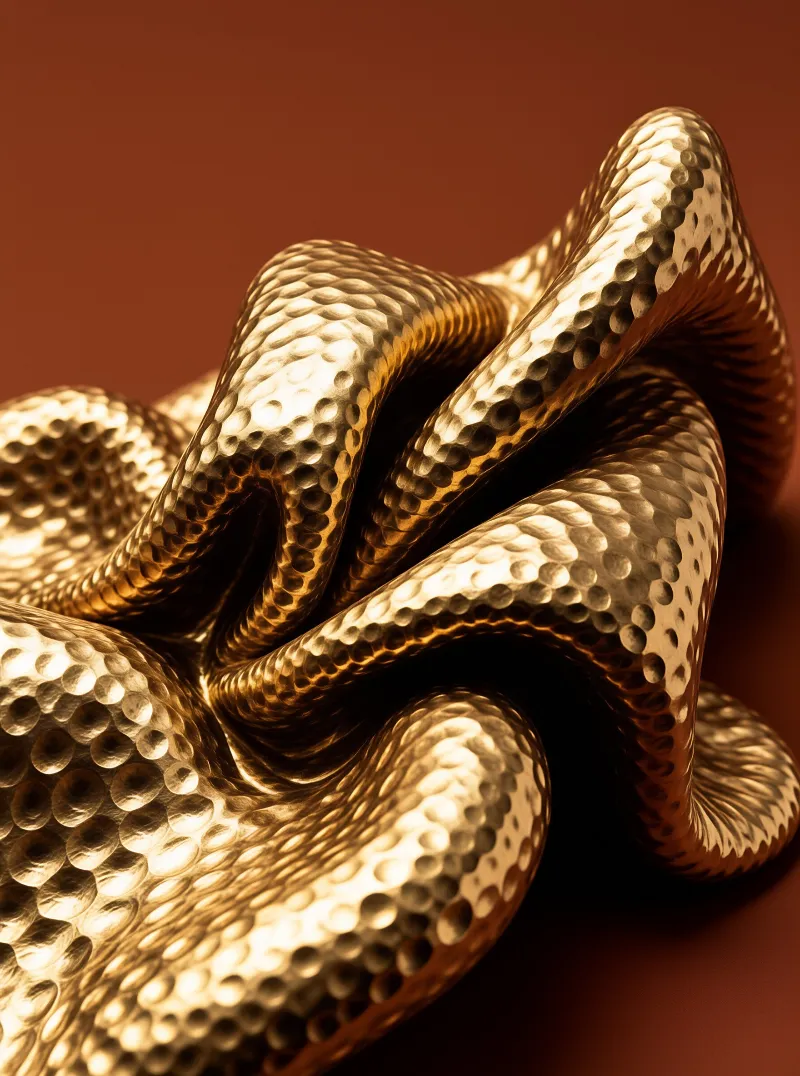 A crumpled ribbon of hammered brass catches warm light against a smooth rust colored surface