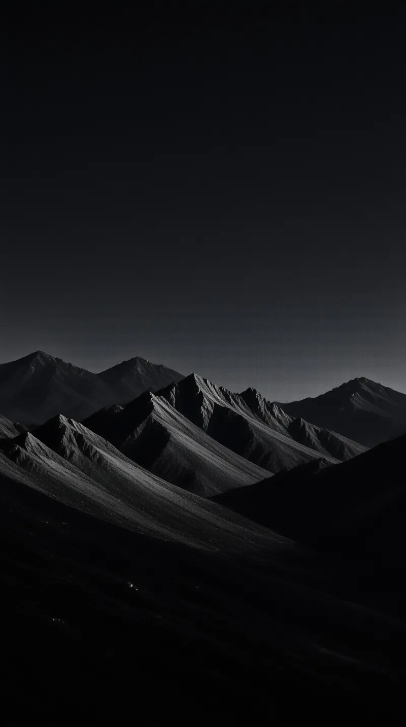 Monochromatic view of layered mountain ranges with sharp ridges casting deep shadows against a dark sky.