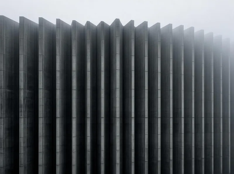 Tall concrete slats extend into thick mist, their uniform vertical lines forming a structured and atmospheric scene with gray tones.