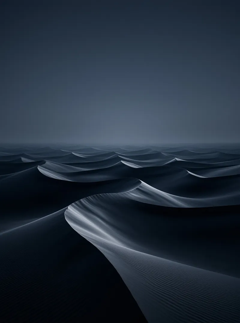 Waves of dark blue sand ripple across a vast desert landscape beneath a dim twilight sky.