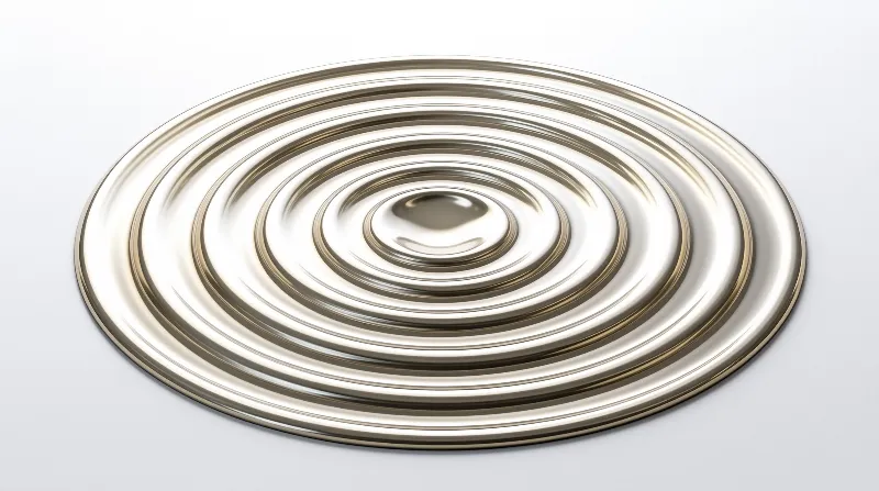 A gold metallic disc with spiral grooves rests on a white surface under bright studio lighting.
