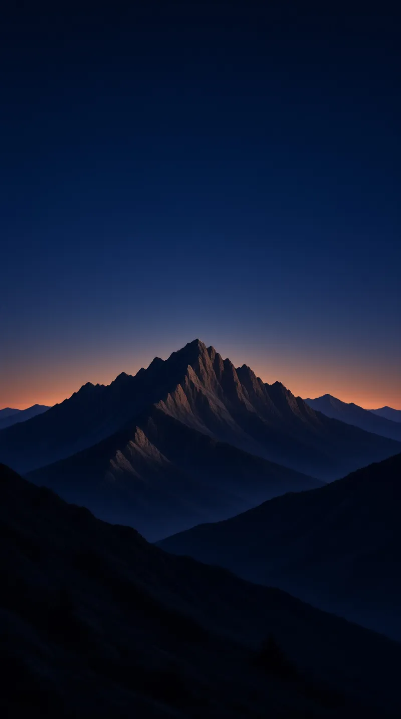 A sharp rocky mountain ridge rises above dark layered lower slopes under a sky that fades from deep indigo to soft warm orange at the horizon