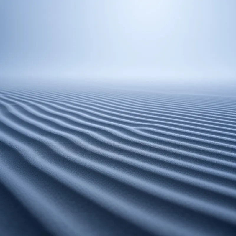 Textured terrain featuring uniform ripples stretching towards blurred horizon where thick fog obscures sky in cool blue tones.
