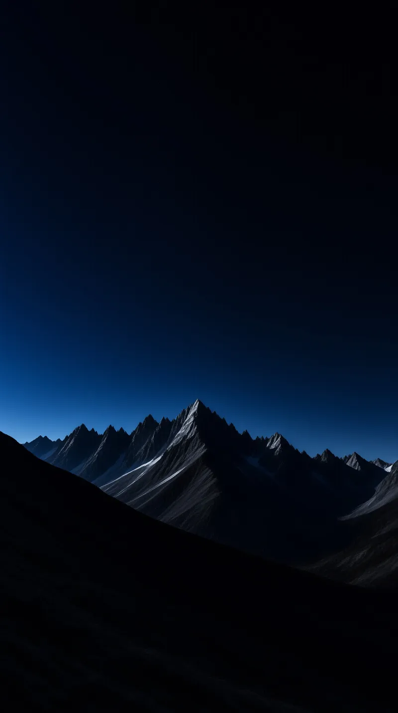Sharp mountain peaks covered with patches of snow rise against a gradient sky that transitions from deep blue near the horizon to black at the top while the foreground remains in deep shadow.
