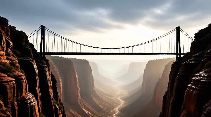 A large suspension bridge is silhouetted against a bright sky while spanning a deep, mist-filled canyon with layered rock walls.