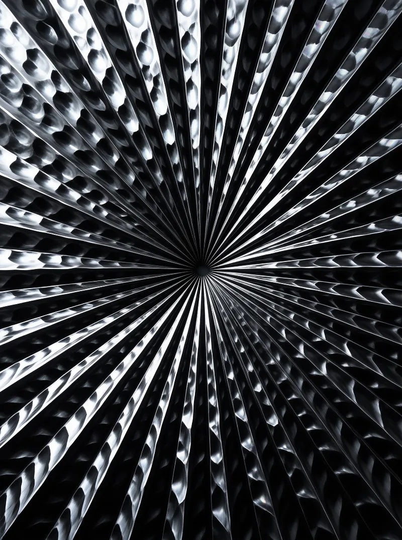 Close up view of textured silver metal sheet where the stamped bumps create radial lines converging towards a central point in a high contrast monochrome composition.