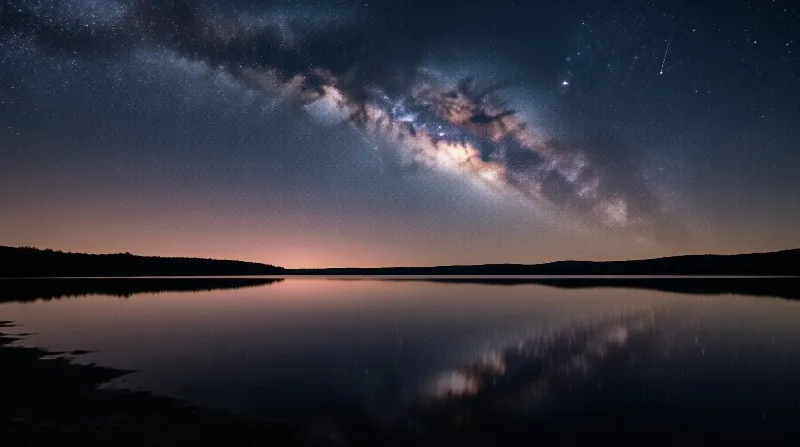 Milky Way galaxy stretches across starry night sky above calm reflective lake with orange horizon glow