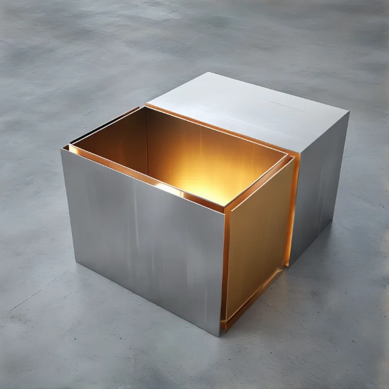 A modern geometric table features a glowing gold interior compartment set beside a solid white block on a grey concrete surface.