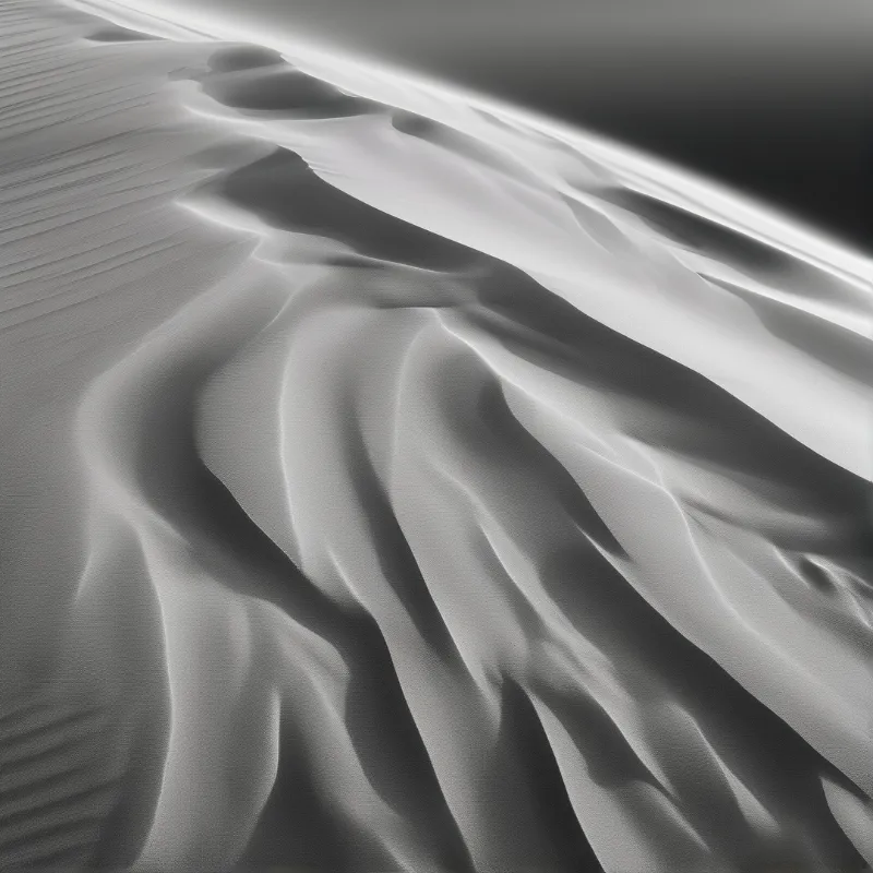 Monochrome view of flowing sand ridges with strong contrast between light and shadow.