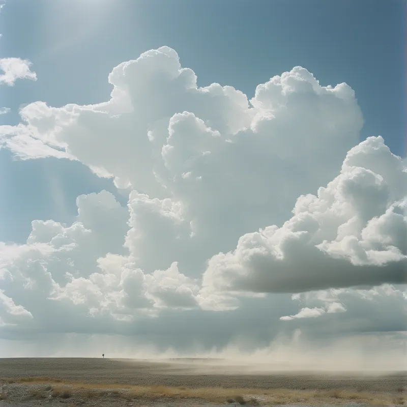 A solitary figure stands on a dusty plain beneath massive white clouds filling the bright sky.