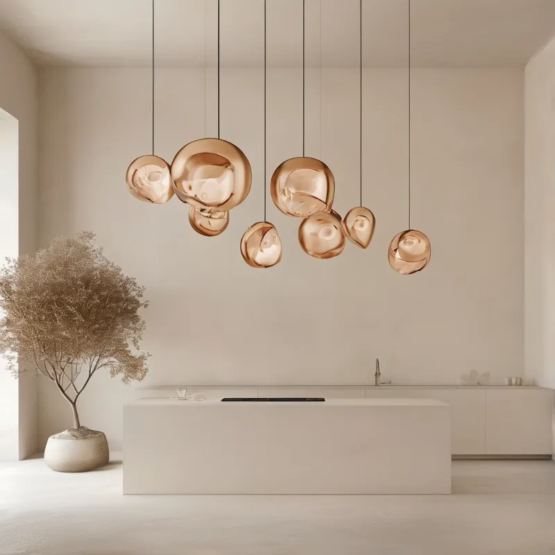 A cluster of copper-toned bubble pendant lights hangs over a sleek white kitchen island in a bright minimalist room.