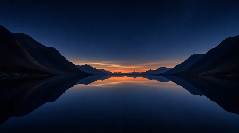 A perfectly calm lake mirrors silhouetted mountains and a warm amber glow along the twilight horizon.