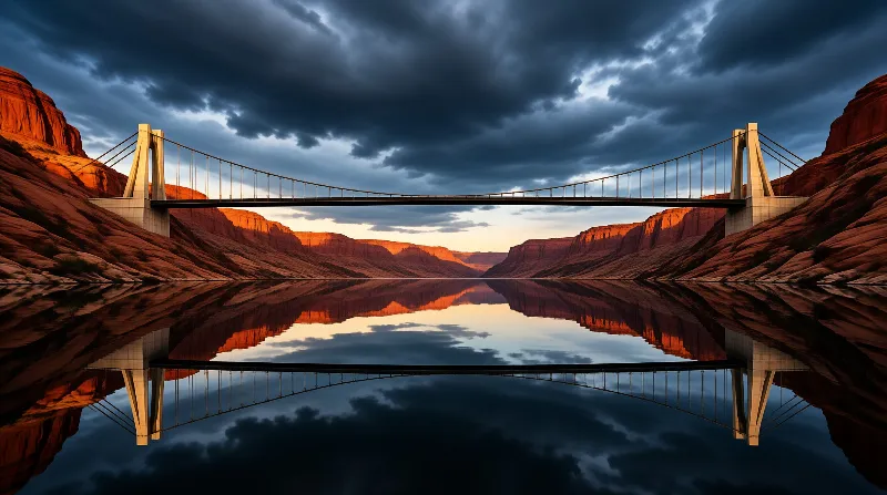 A modern suspension bridge spans a calm river in a red rock canyon, its full reflection mirrored under a dramatic stormy sky.