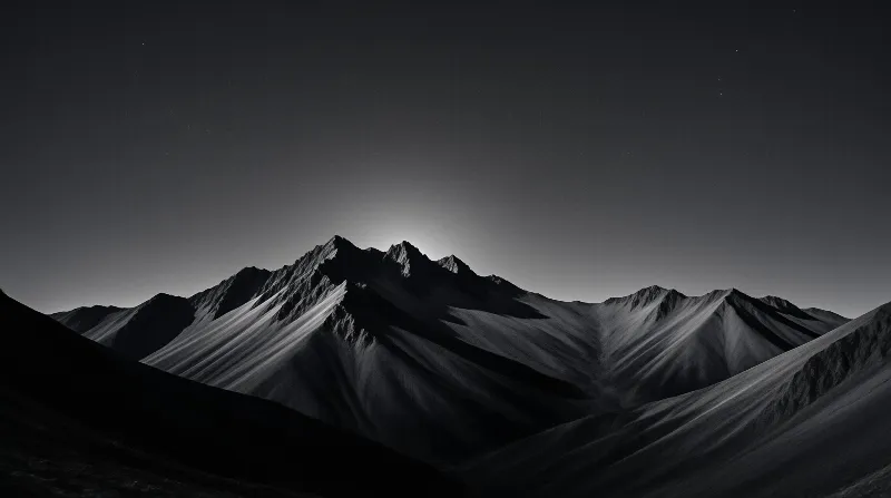 A monochrome landscape captures jagged mountain peaks where strong lighting creates deep shadows across the slopes beneath a star-filled night sky.