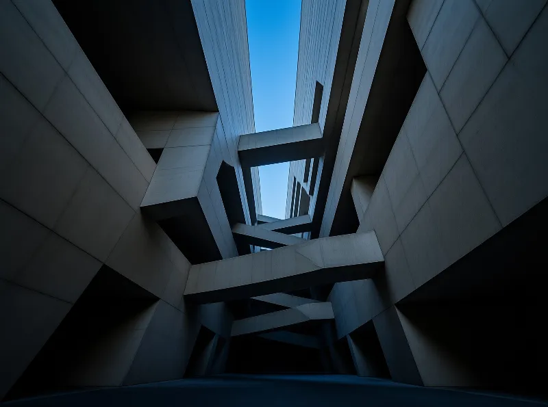 Low angle view of intersecting concrete beams in a brutalist structure looking up at a clear blue sky.