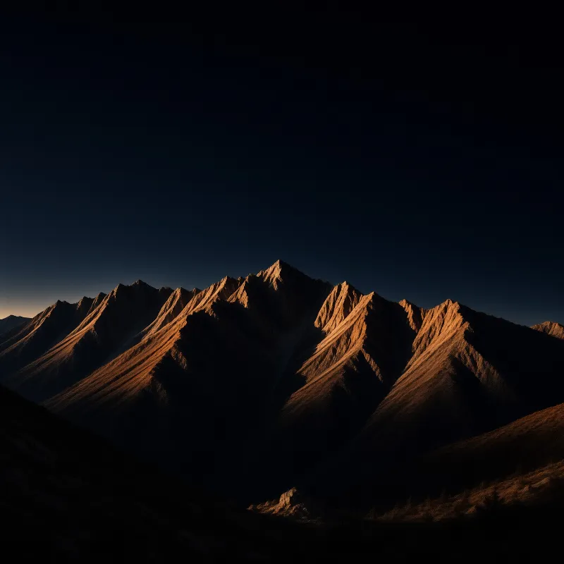 A jagged mountain crest glows amber in low sun, its shadowed slopes falling away beneath a vast dark blue sky.