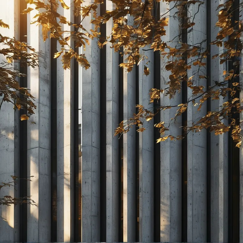 Vertical concrete fins cast long shadows, with golden autumn leaves in the foreground catching sunlight.