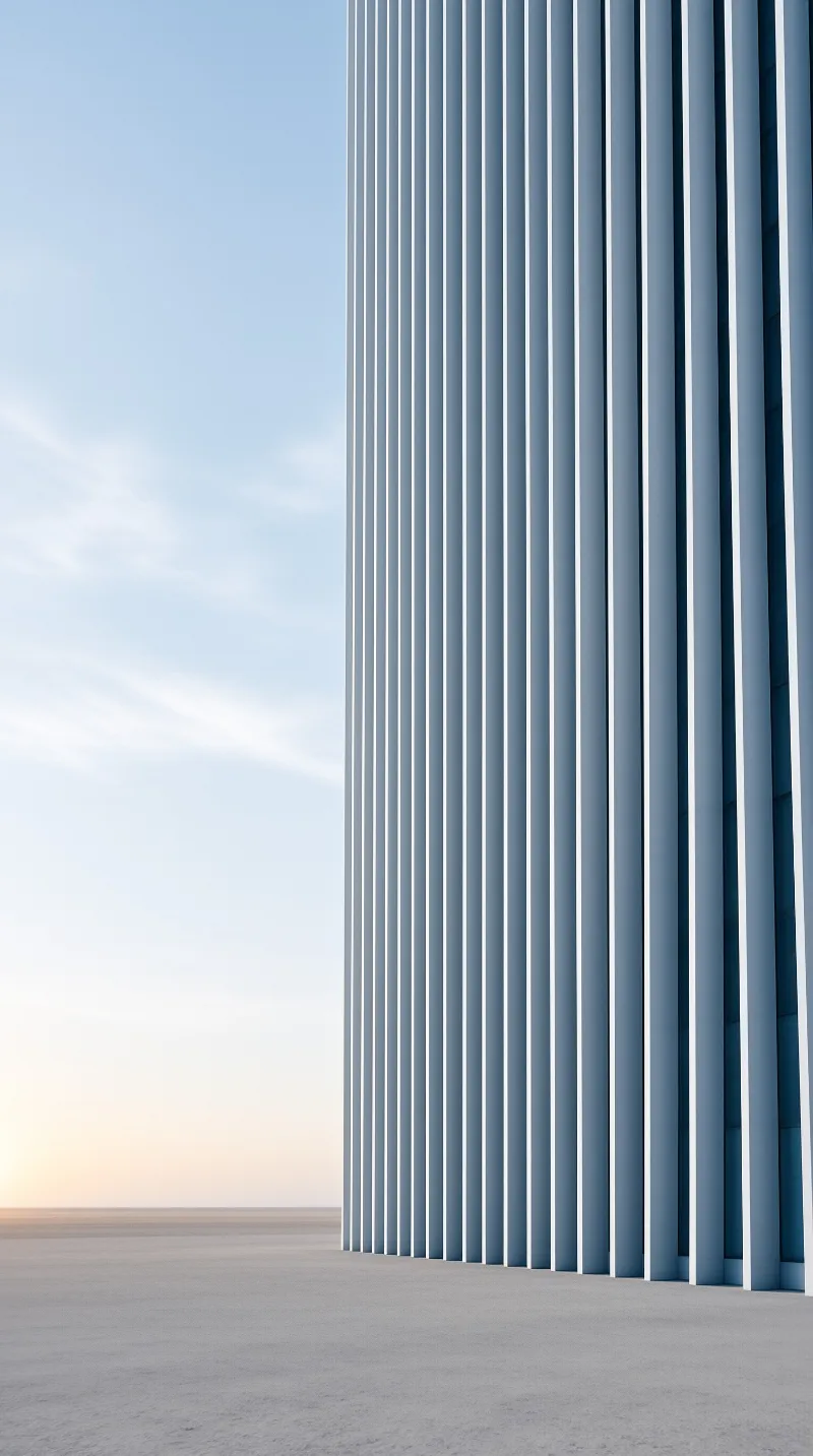A tall structure with repeating white vertical fins stands beside empty ground under a soft gradient sky.
