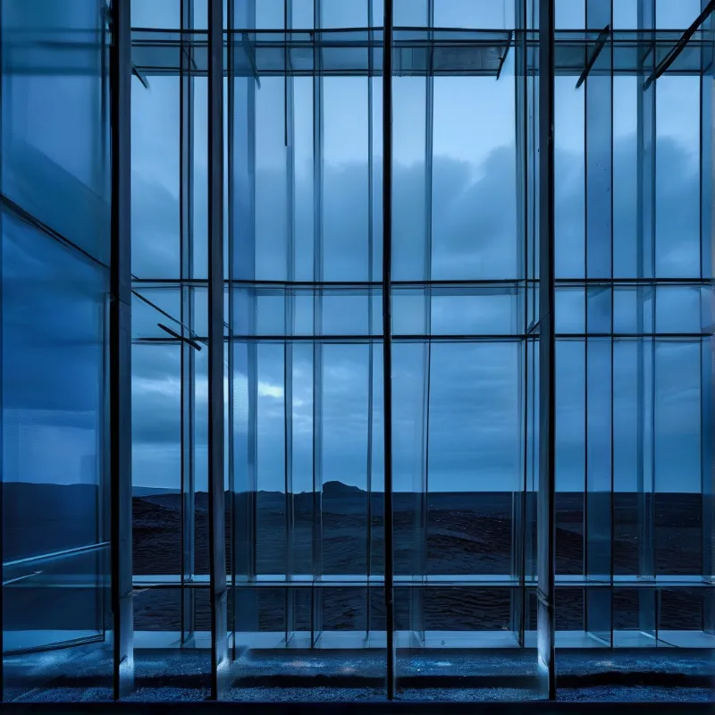 A large glass window structure reflects a dark blue sky over distant hills during the evening twilight hours.