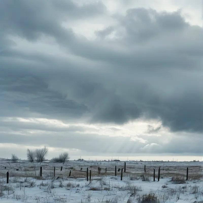 A vast snow covered plain stretches toward the horizon beneath heavy grey clouds, featuring scattered wooden fence posts and visible sunbeams cutting through the gloom.