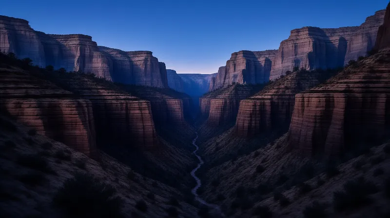 A winding river flows through a massive canyon while steep rocky cliffs rise on both sides under a deep blue sky.