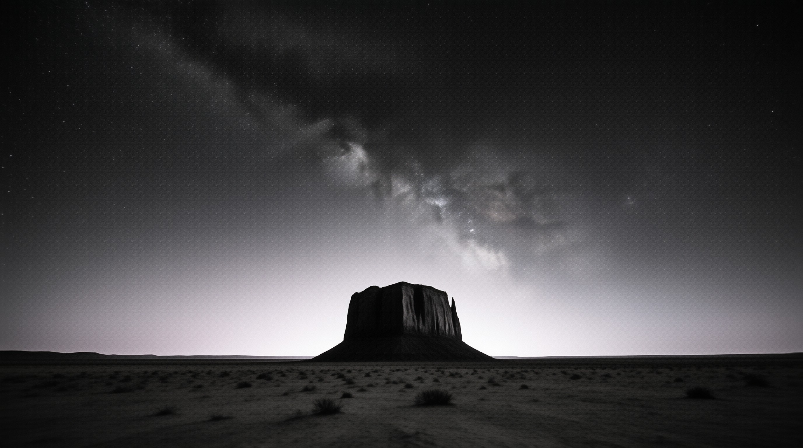 A solitary mesa rises from the desert plain beneath a vast starry sky filled with the Milky Way.