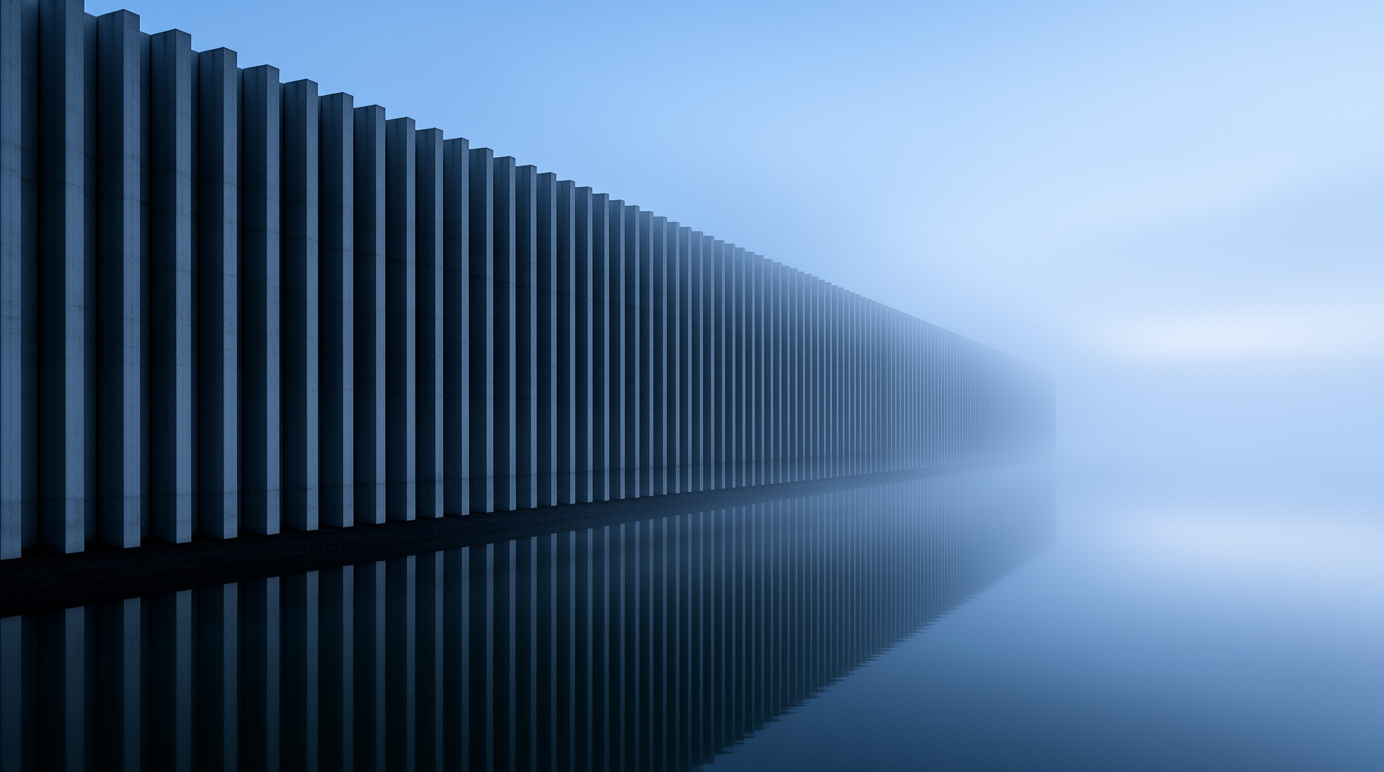 Vertical dark pillars recede into blue fog, casting a sharp reflection on the calm water surface.