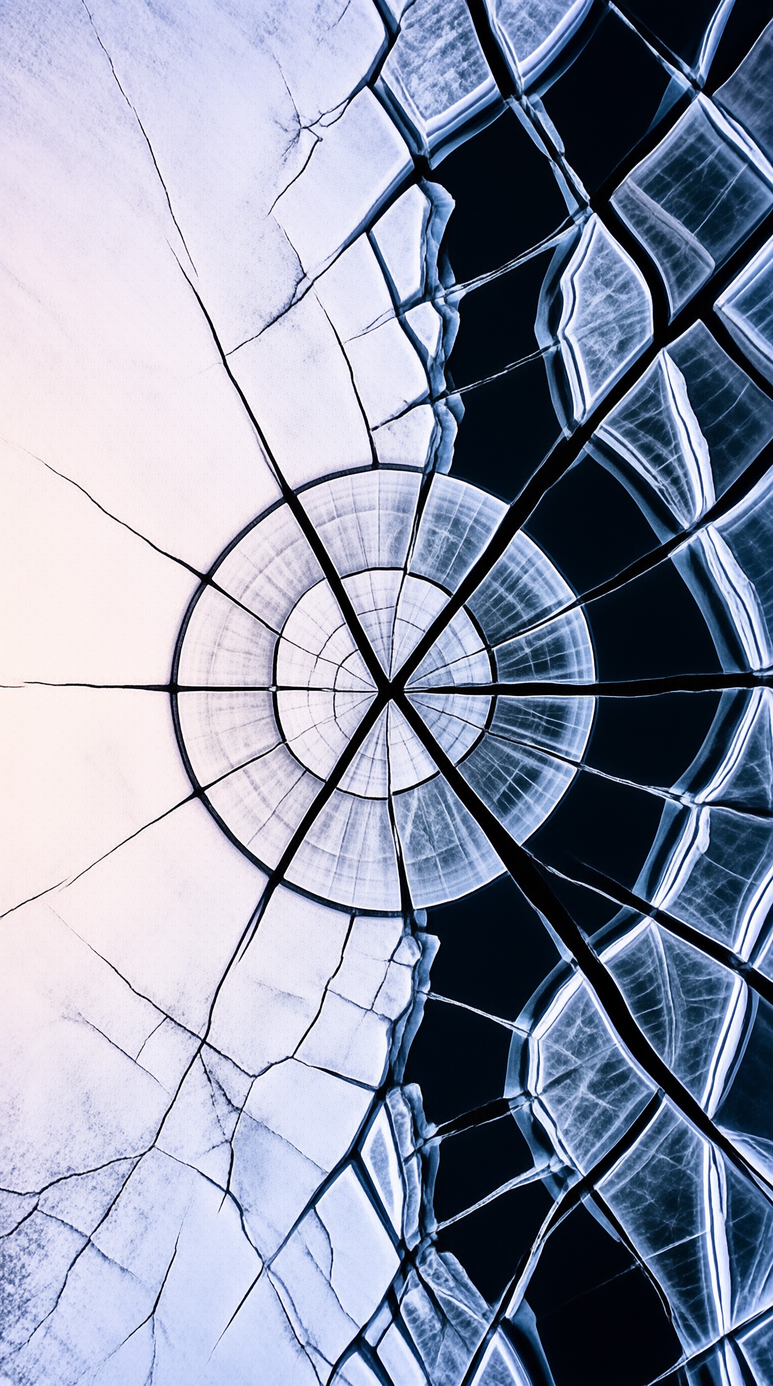 Fine fractures spread outward from a bright bullseye across a pane of blue and cream broken glass