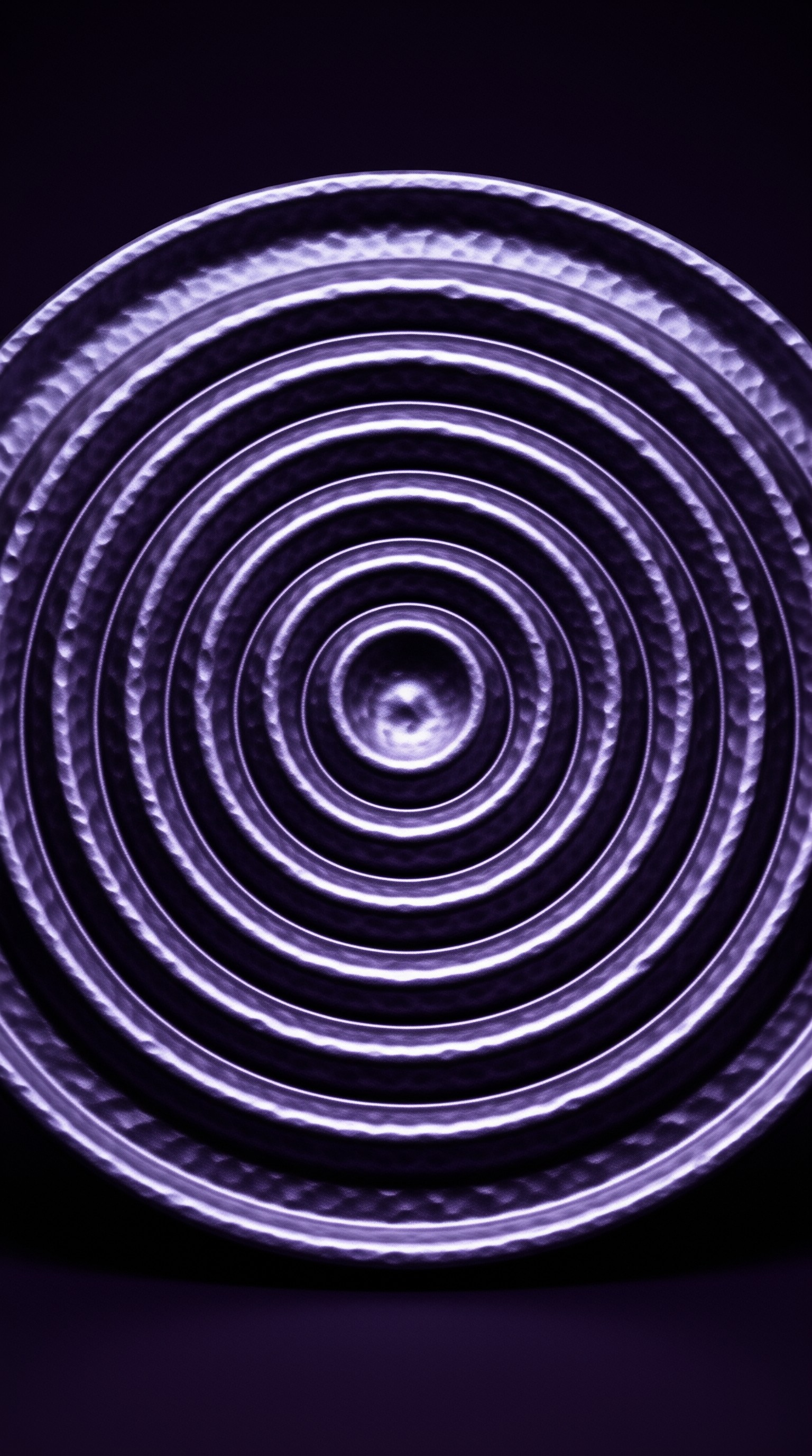 Hammered metal circles spread outward in glowing violet tones, echoing ripples across a shadowed plane.