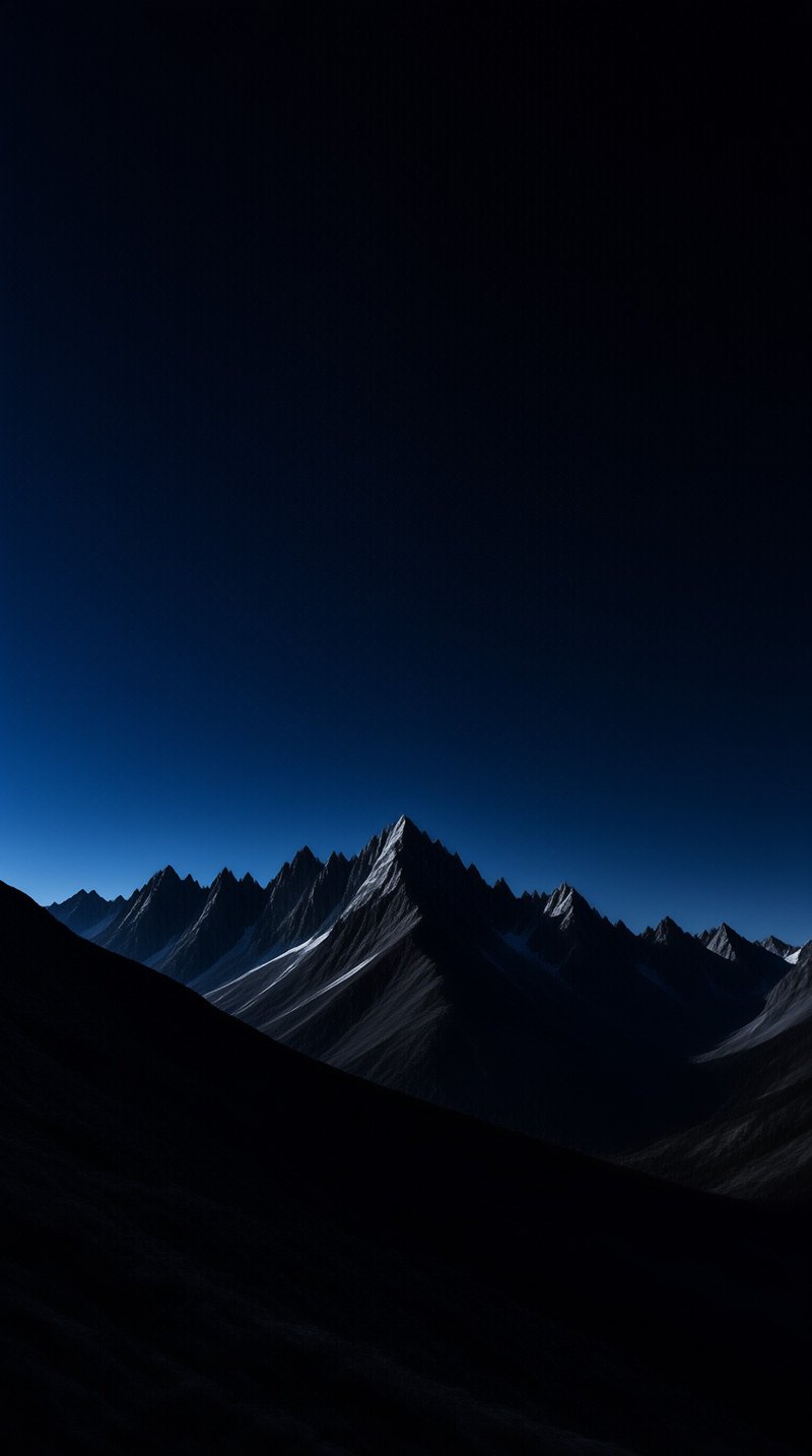 Sharp mountain peaks covered with patches of snow rise against a gradient sky that transitions from deep blue near the horizon to black at the top while the foreground remains in deep shadow.