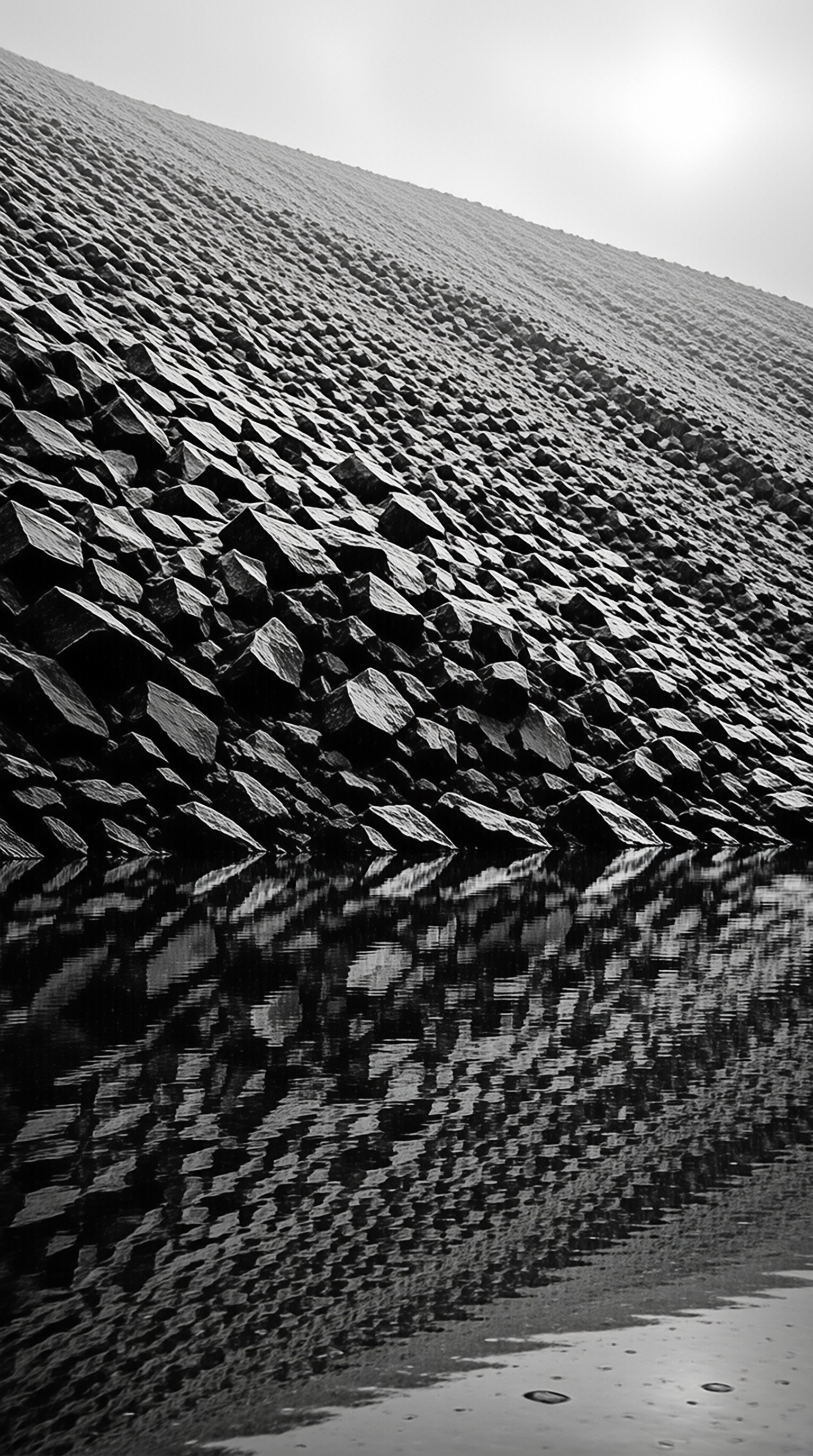 Rows of dark stone structures slope down toward the water creating a strong diagonal composition in monochrome tones.