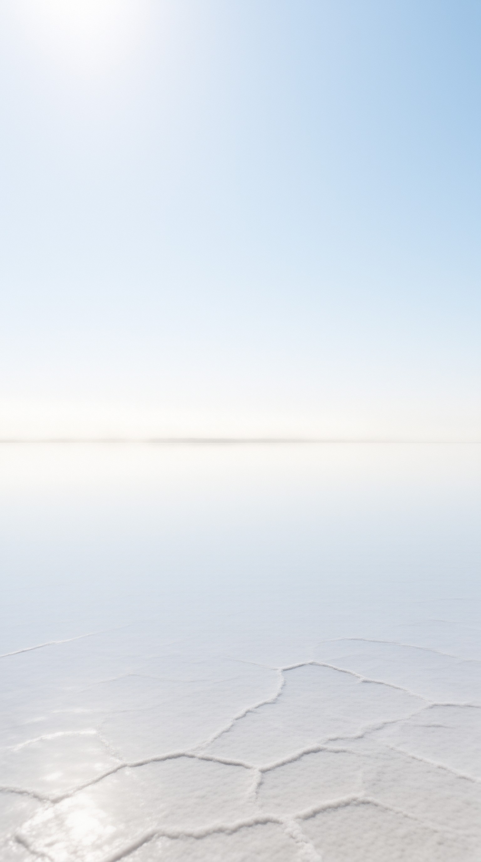 A vast white salt crust breaks into geometric plates under a soft gradient of morning sky.