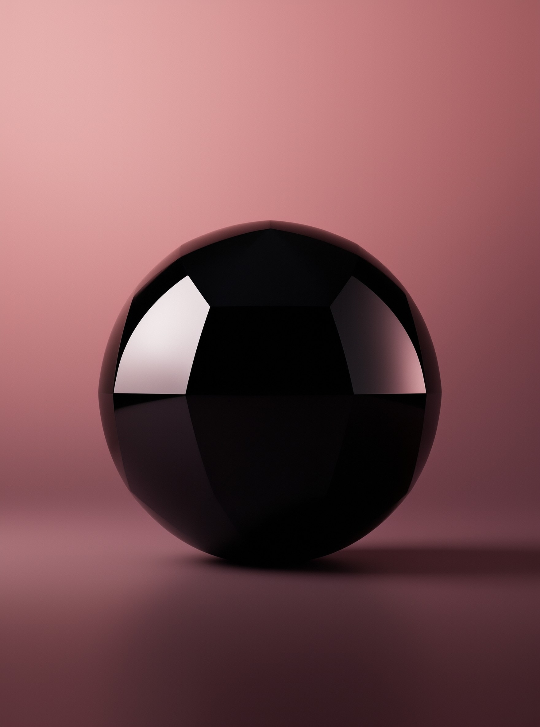 A glossy black sphere rests against a gradient pink background showing sharp white reflections on its curved surface.