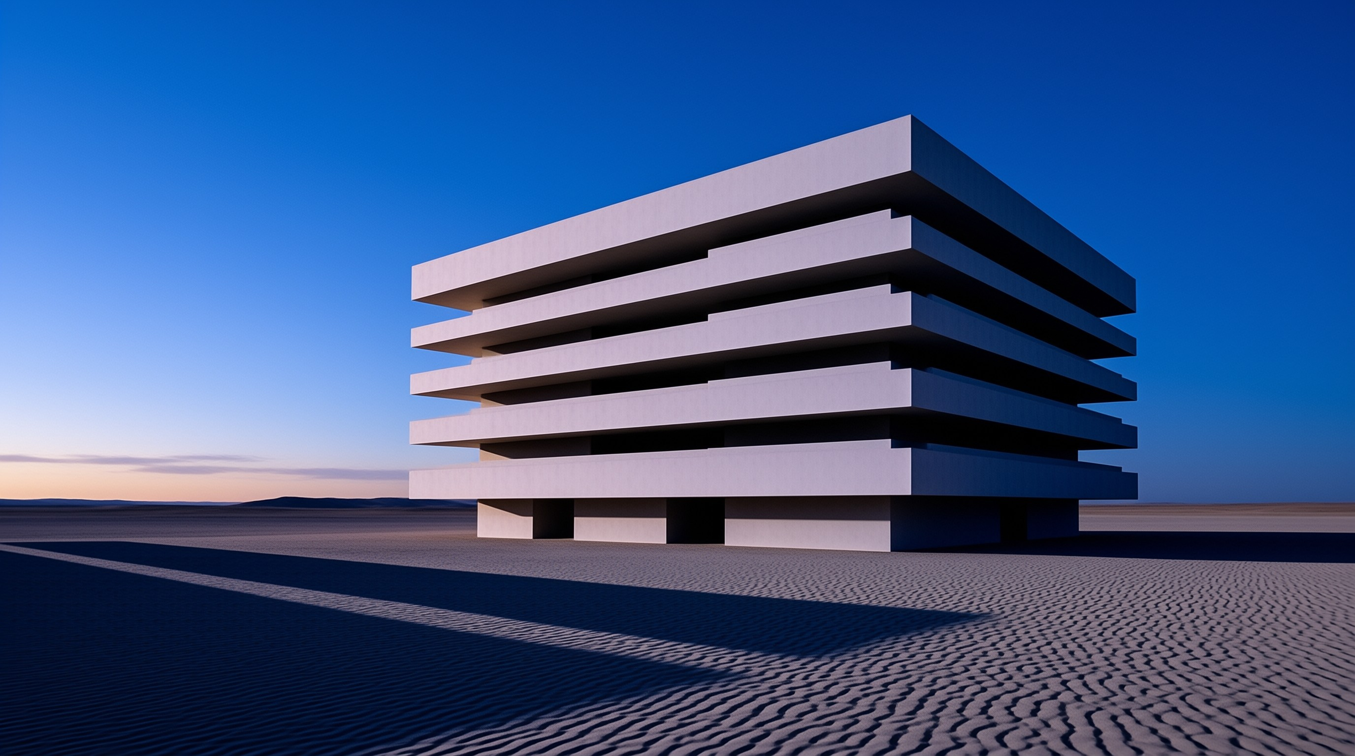A white layered building stands alone on sandy ground under a deep blue sky during twilight.